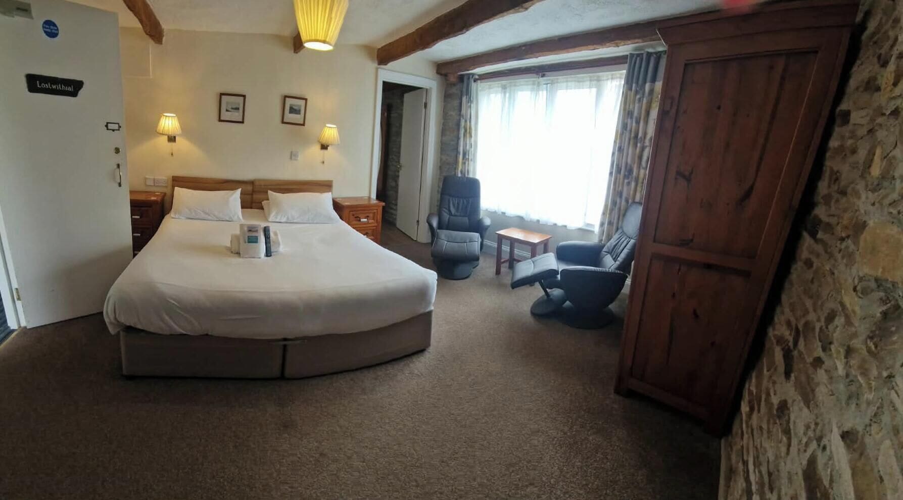 Una habitación de hotel con una cama grande, una silla, una mesita y un armario.