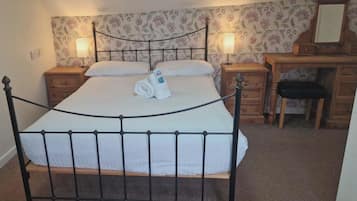 A bed with a metal frame, a wooden nightstand with a lamp, a wooden dresser, and a mirror.