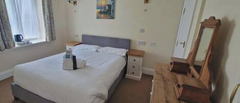 A hotel room with a bed, bedside tables, a dresser, a painting on the wall, and a window with curtains.