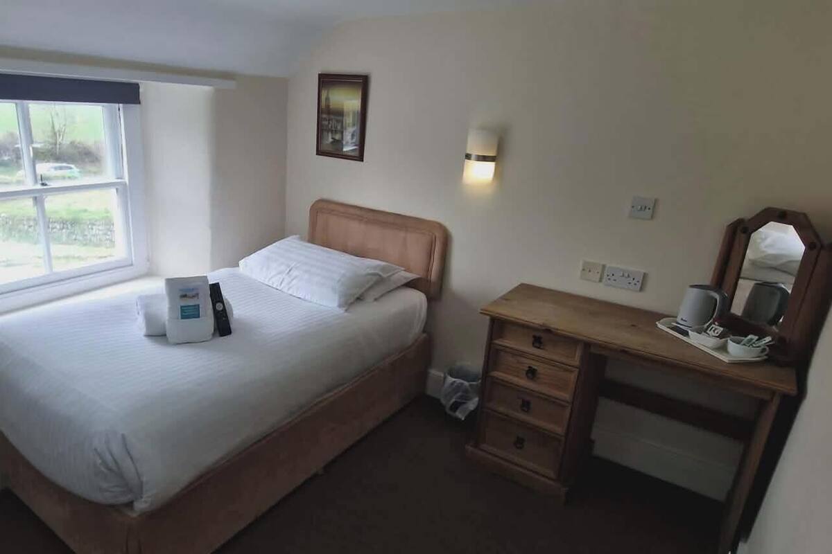 A bedroom with a bed, a desk, a chair, a window, and a wall-mounted light.