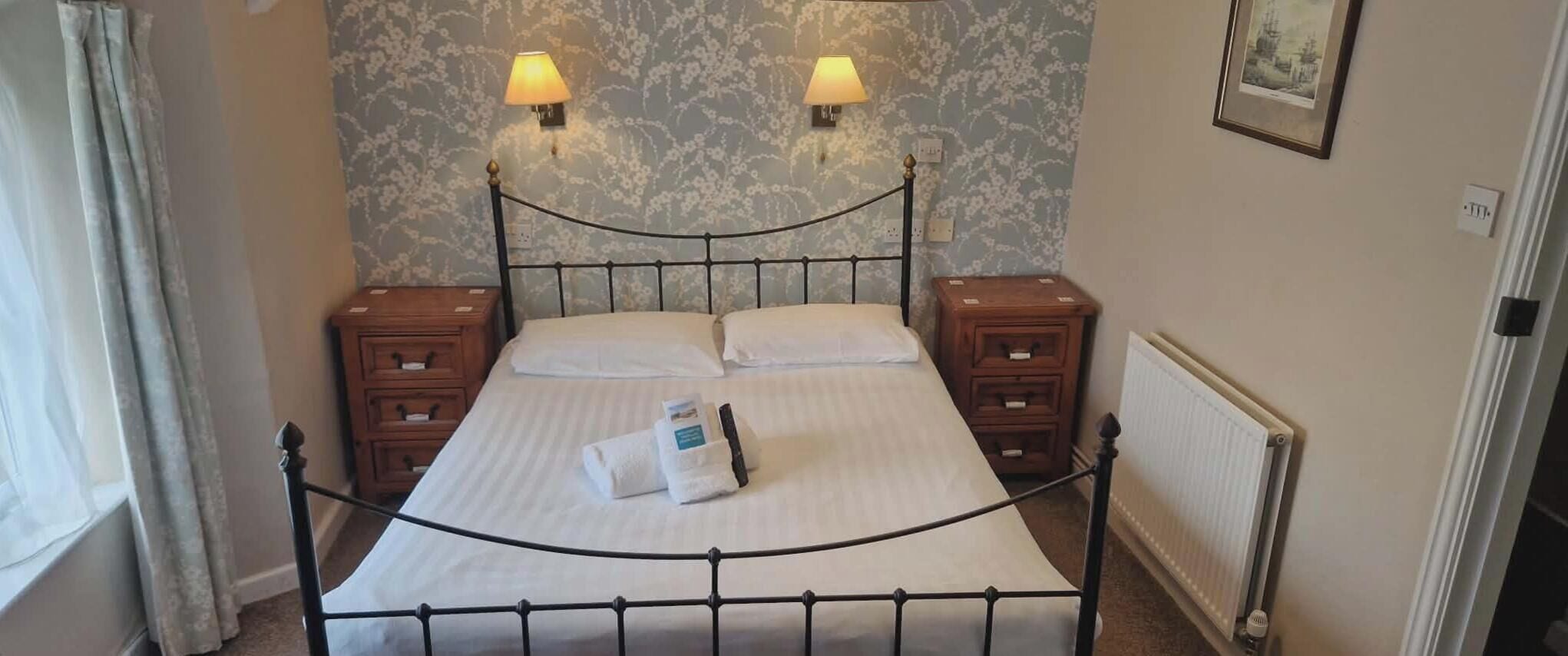 Un lit bien fait, avec du linge de lit blanc, deux lampes de chevet, une table de chevet en bois et un radiateur.