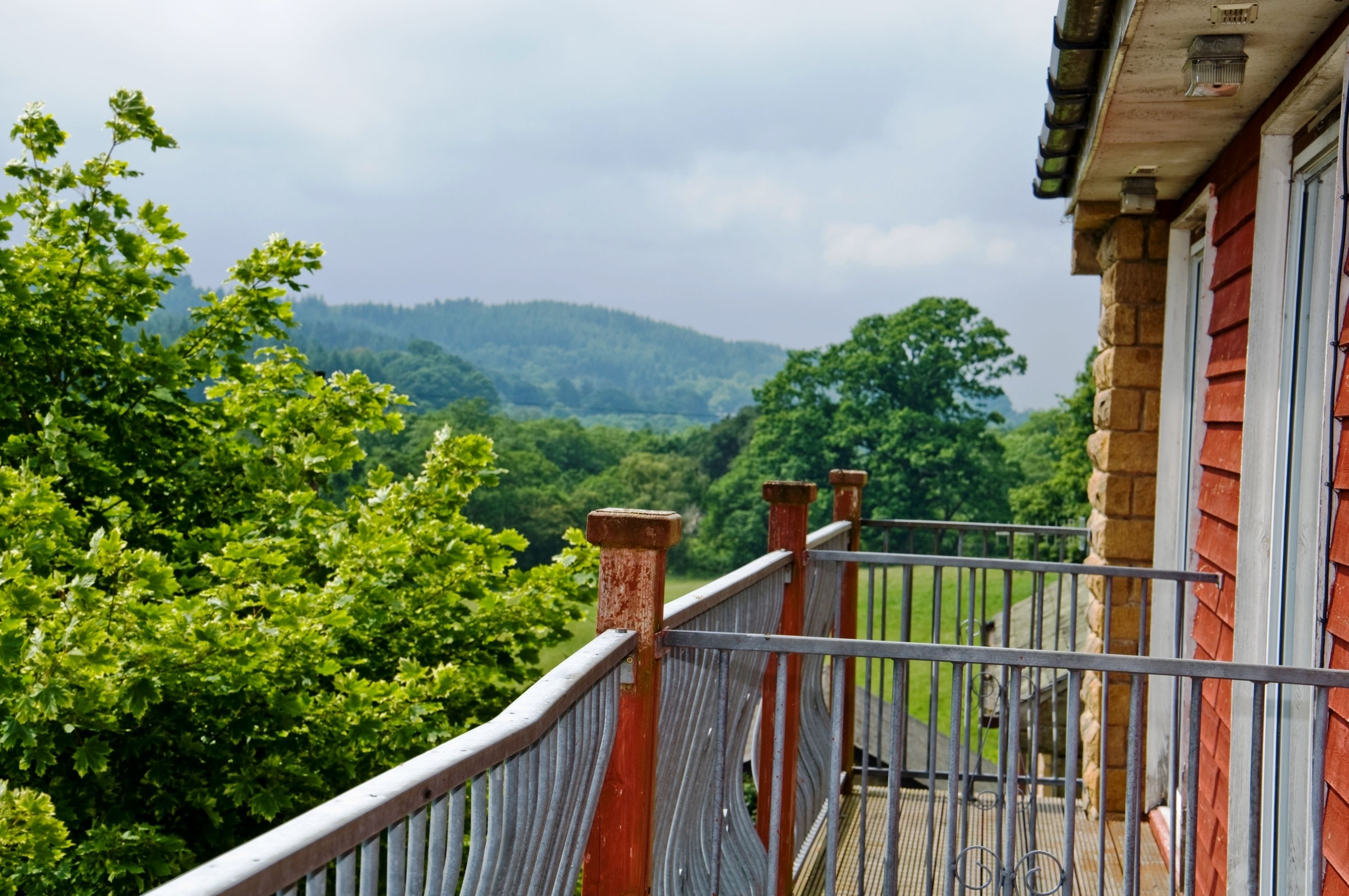 A balcony with a view of a lush green landscape and distant hills.