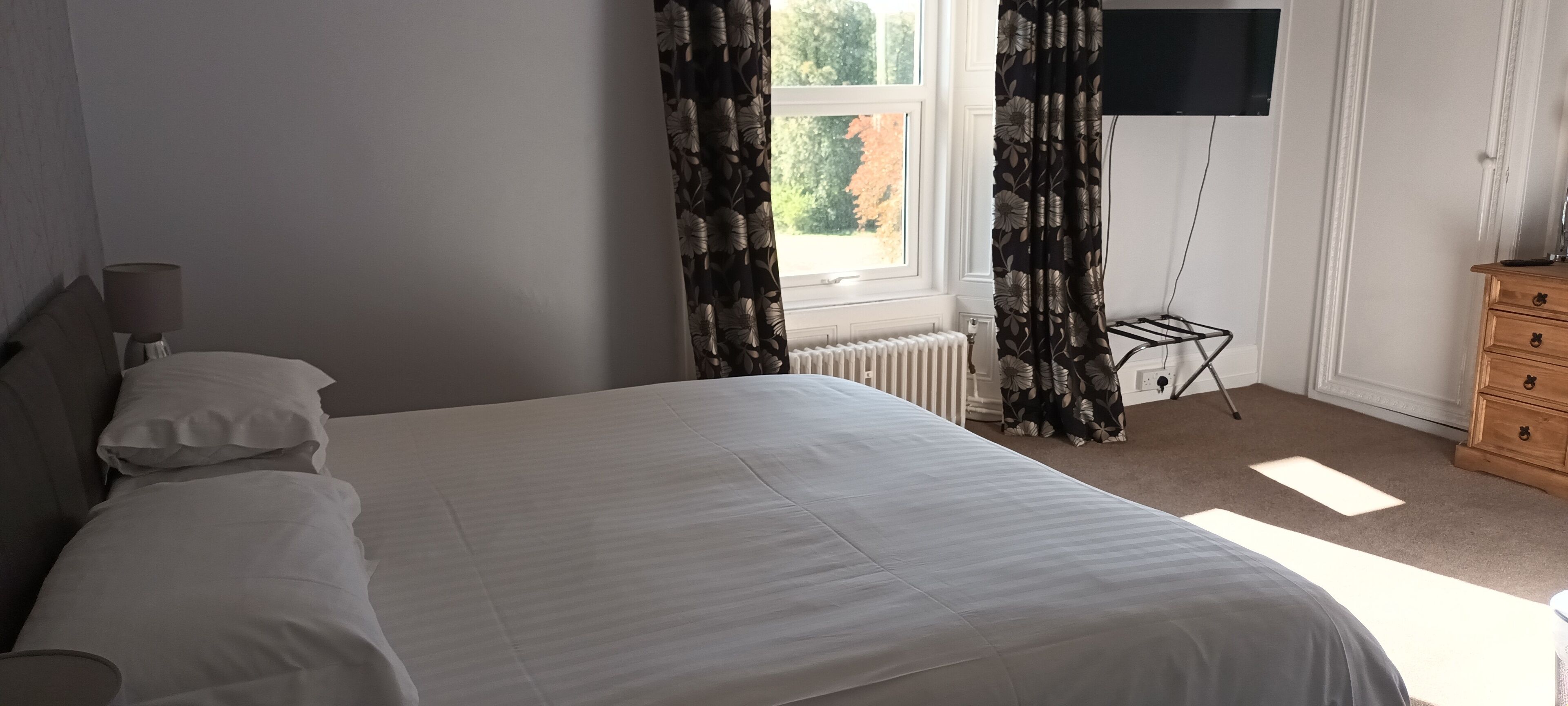 A bedroom with a bed, a nightstand, a dresser, a radiator, and a window with curtains.