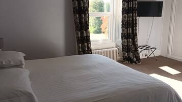 A bedroom with a bed, a nightstand, a dresser, a radiator, and a window with curtains.