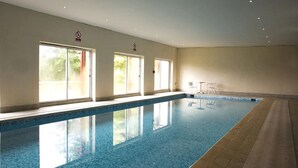 An indoor swimming pool with clear glass walls, a tiled floor, and a few chairs near the pool. - Riverdale Hall Hotel (Hexham)