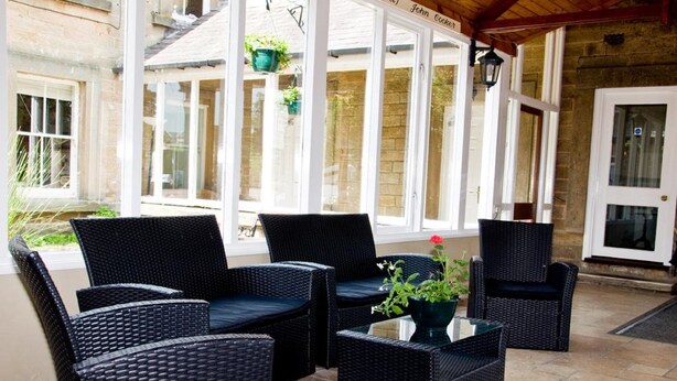 A covered patio area with wicker furniture and a potted plant. - Riverdale Hall Hotel (Hexham)