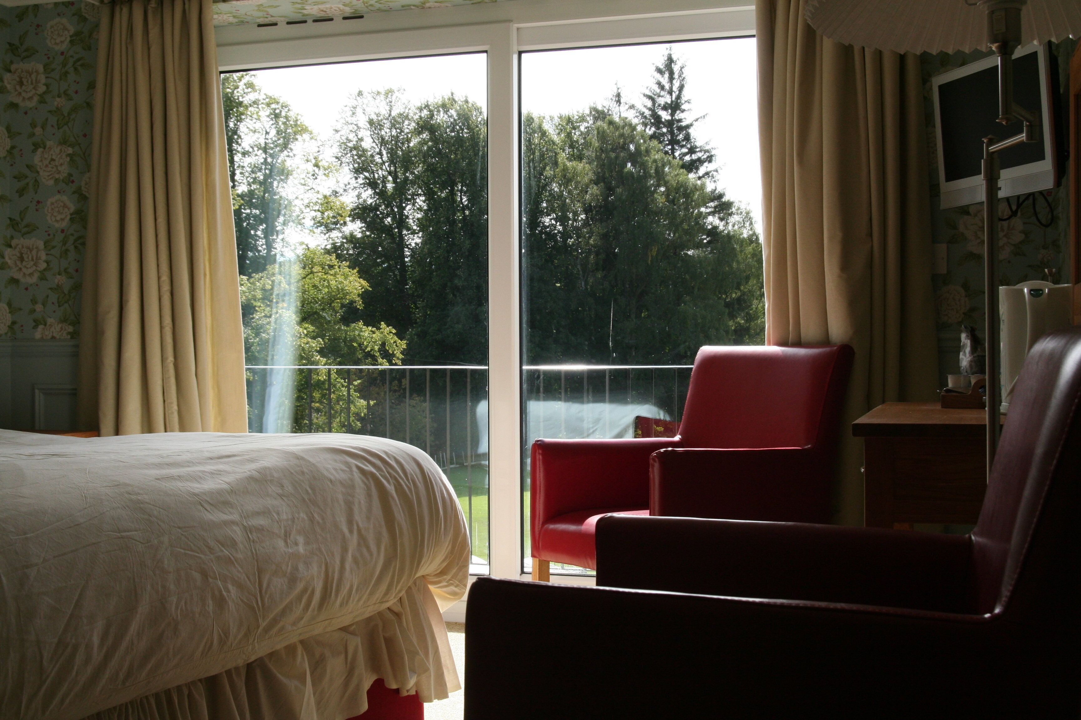 Un dormitorio con una cama, una silla roja y vistas a árboles a través de un ventanal amplio.