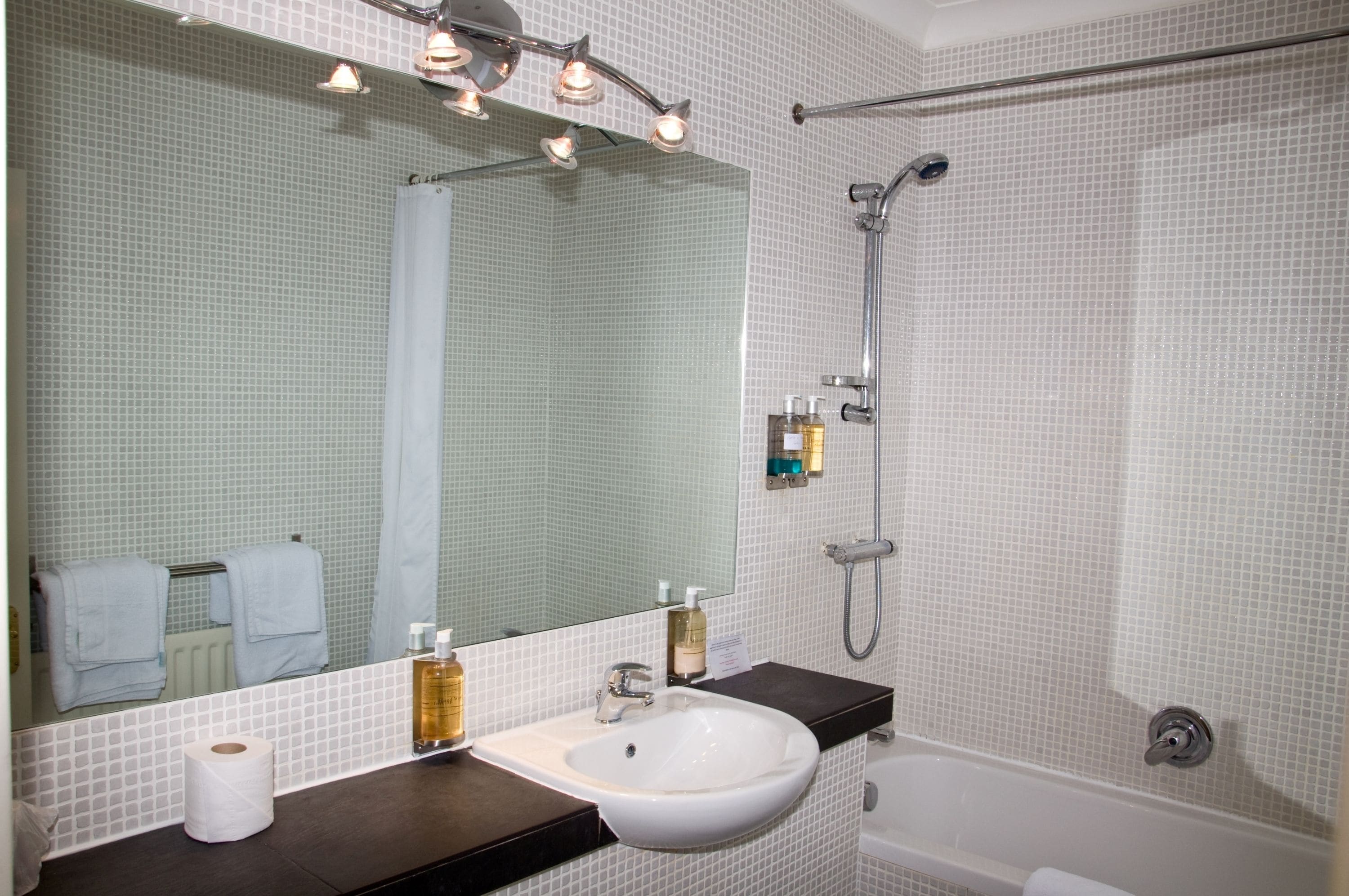 A bathroom with a white sink, a mirror, a shower, and a towel rack.