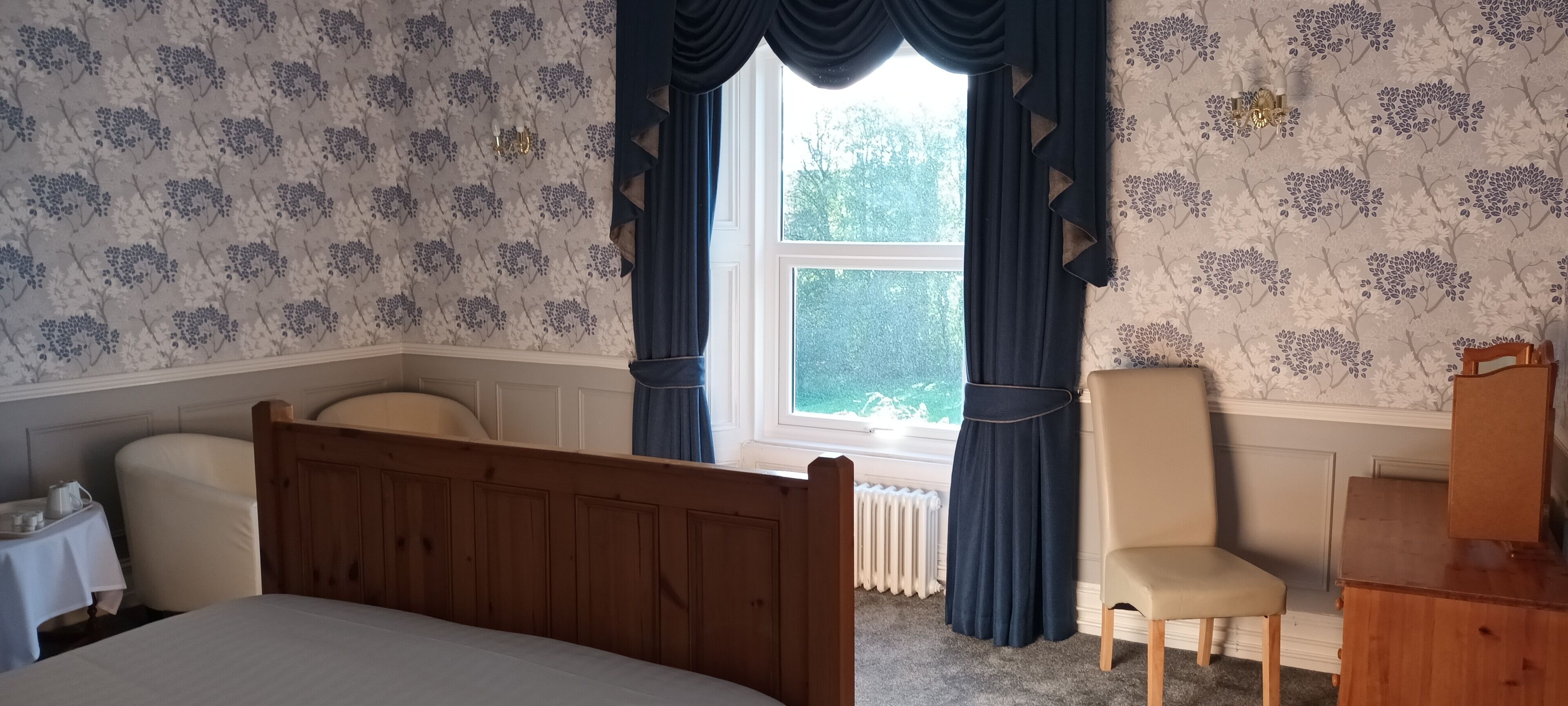 A bedroom with a wooden bed, a chair, a dresser, and a window with curtains.