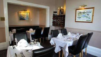 A dining area with tables set for a meal, a wine rack, and two framed artworks on the walls.