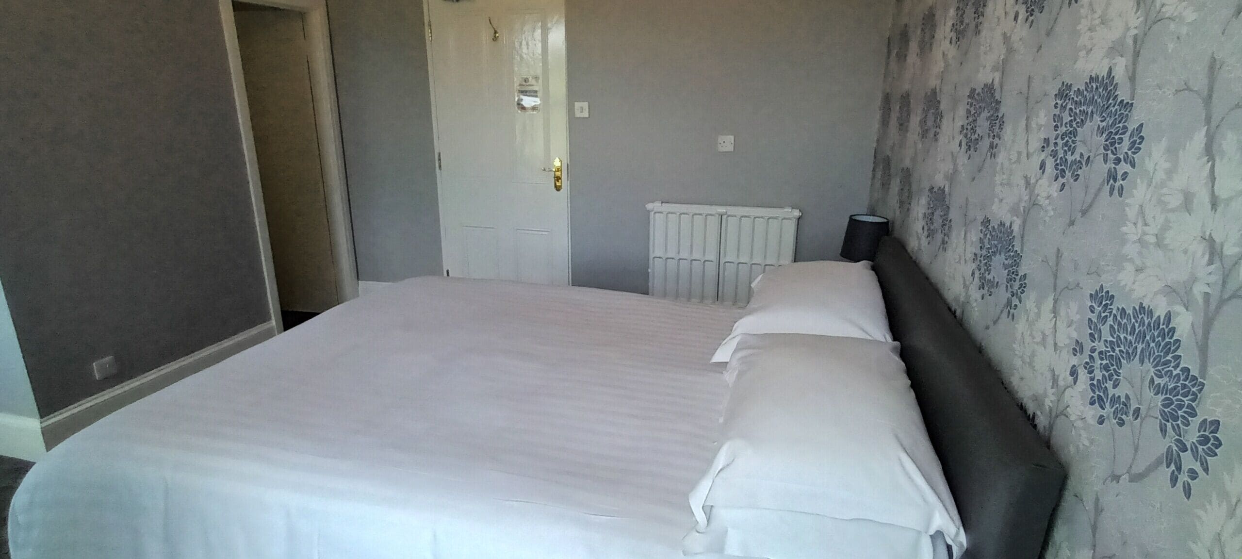 A bedroom with a large bed, a radiator, and a door leading to another room.