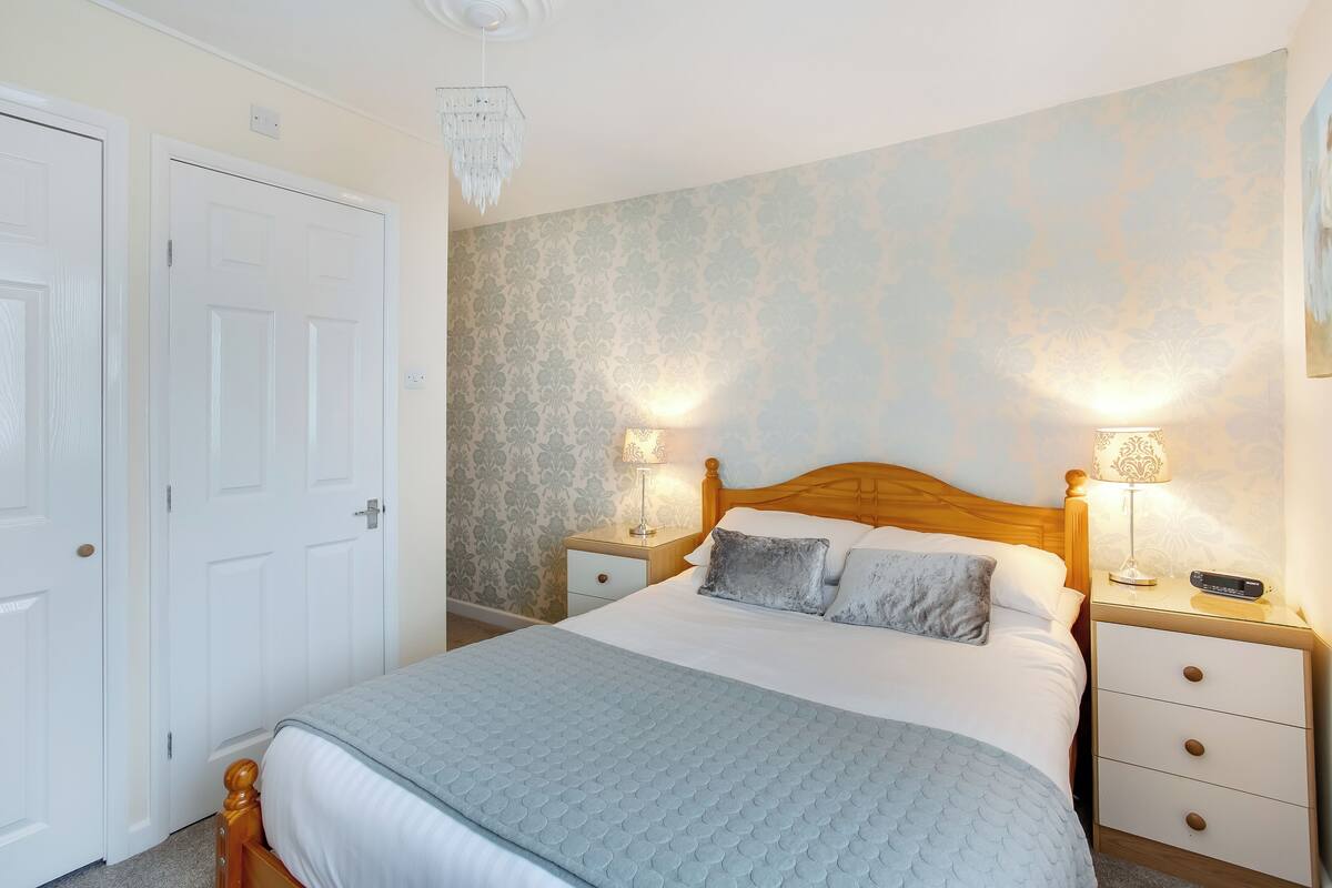 A neatly arranged bedroom with a bed, two bedside tables, a nightstand, and a chandelier.