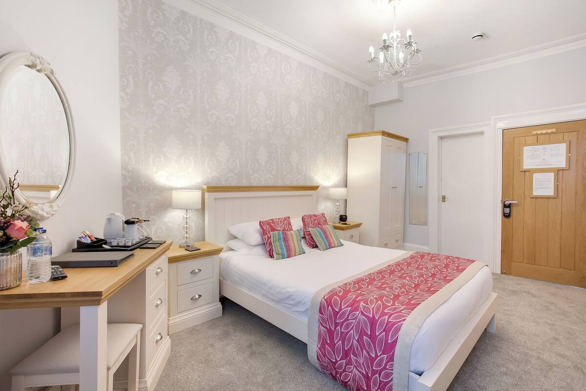 A neatly arranged bedroom with a bed, bedside tables, a desk, and a mirror.