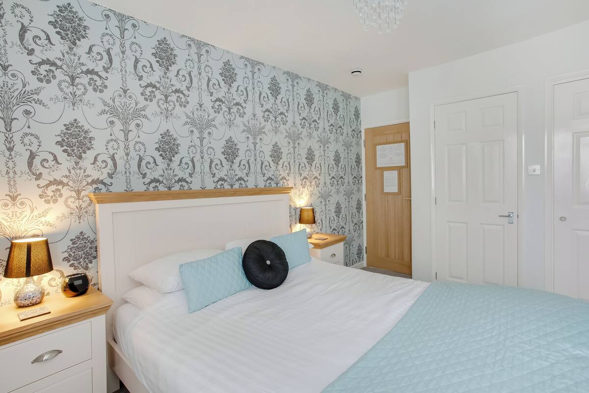 A neatly made bed with a quilted cover, two bedside lamps, and a nightstand with a vase and a remote control.