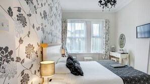 A neatly arranged bedroom with a bed, bedside table, lamp, and a view of the outside through a window.