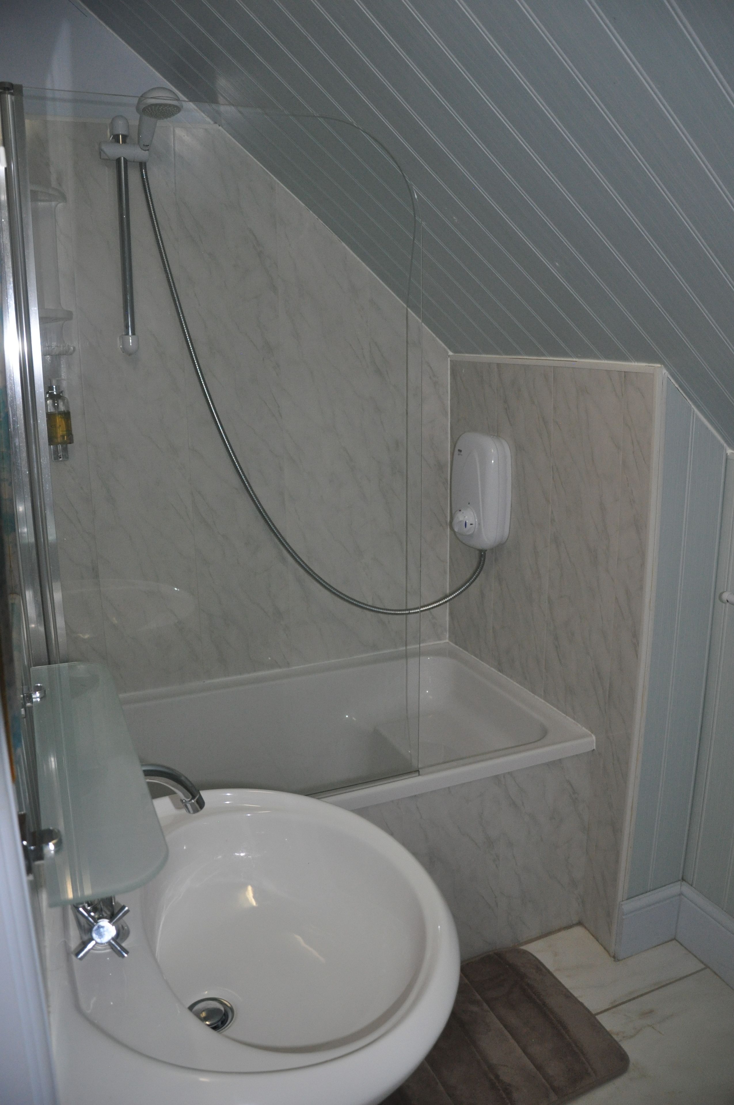 Un baño con ducha envuelta en vidrio, un lavamanos blanco y un revestimiento de mármol en la pared.