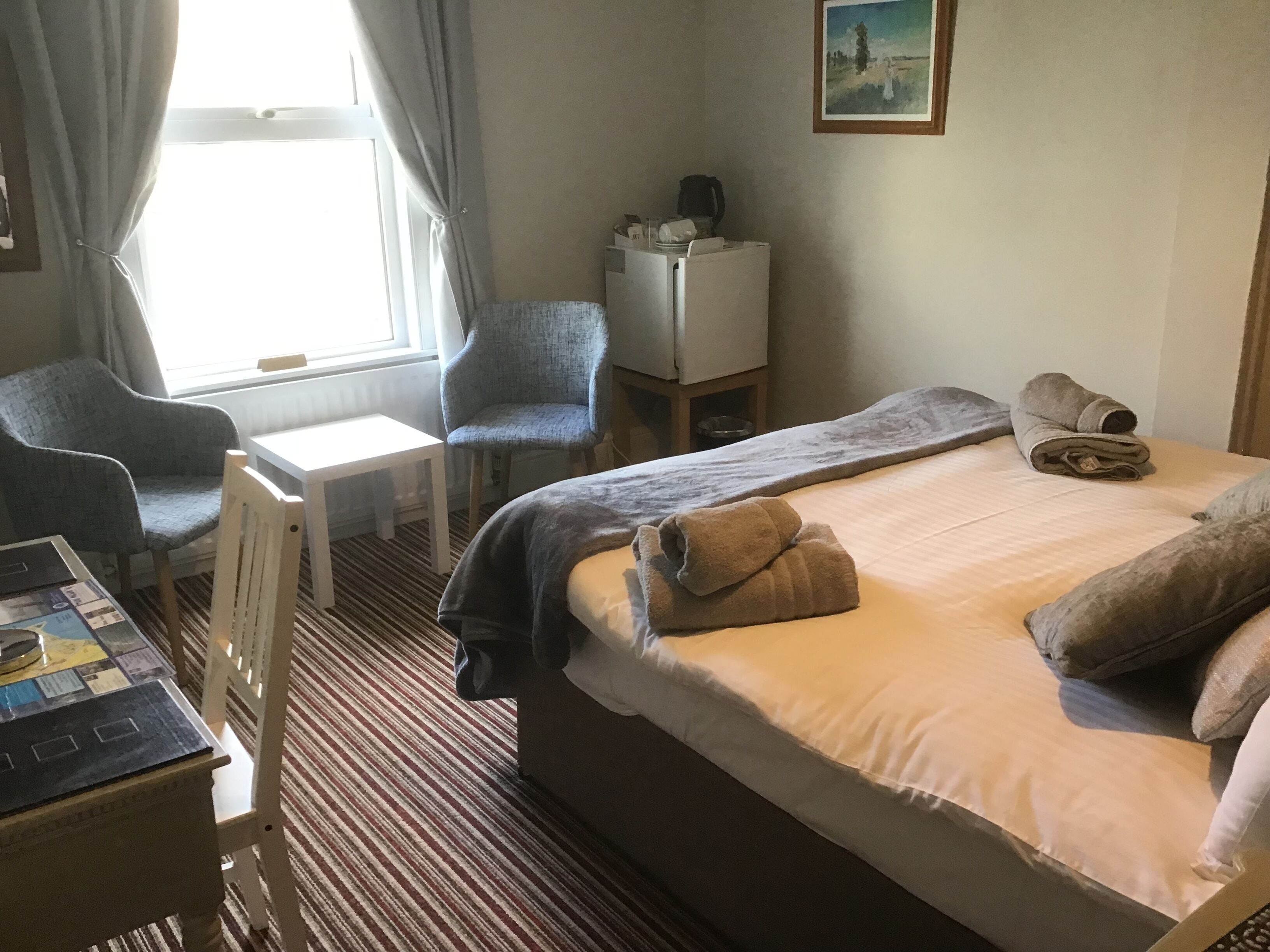 A hotel room with a bed, two chairs, a small table, and a desk.