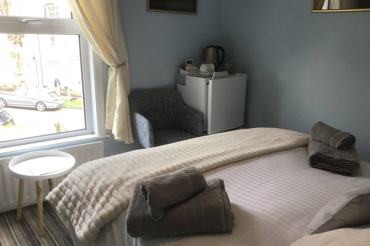 A hotel room with a bed, a chair, a small table, and a window with curtains.