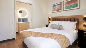 A neatly arranged bedroom with a large bed, a bedside table, a nightstand, a mirror, and two framed pictures on the wall. - Mia Mia House in the Desert (Newman)