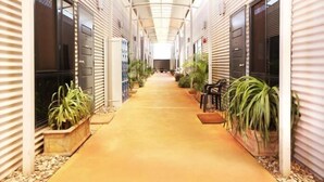 A corridor with a tiled floor, flanked by potted plants and a series of doors on either side. - Mia Mia House in the Desert (Newman)