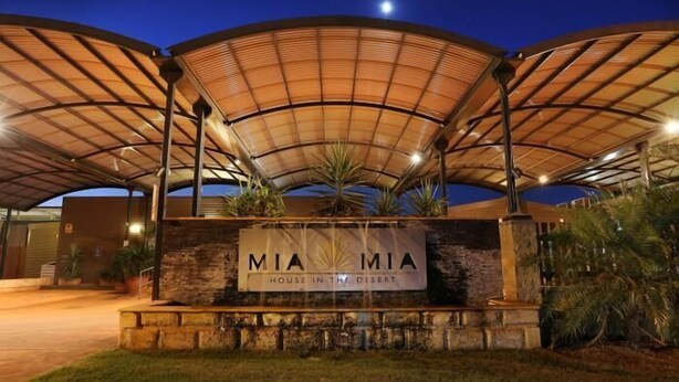 A building with a large, arched roof structure and a sign that reads "MIA House in the Desert." - Mia Mia House in the Desert (Newman)