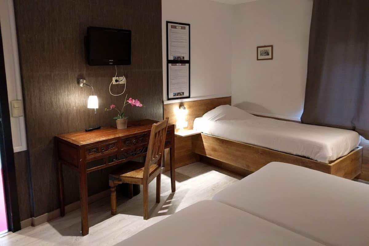 Quarto de hotel com uma escrivaninha de madeira, uma cadeira, uma cama e uma televisão na parede.