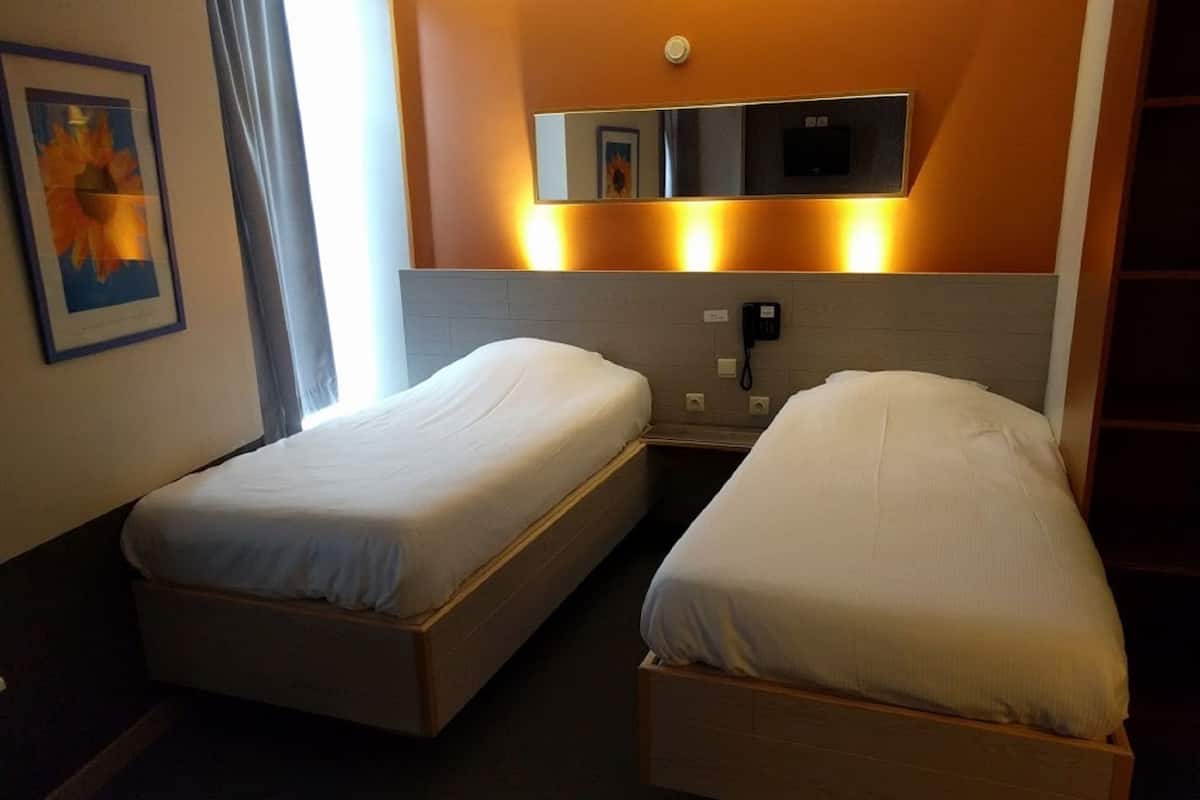 Quarto de hotel com duas camas de solteiro, telefone de apoio e espelho fixado na parede.