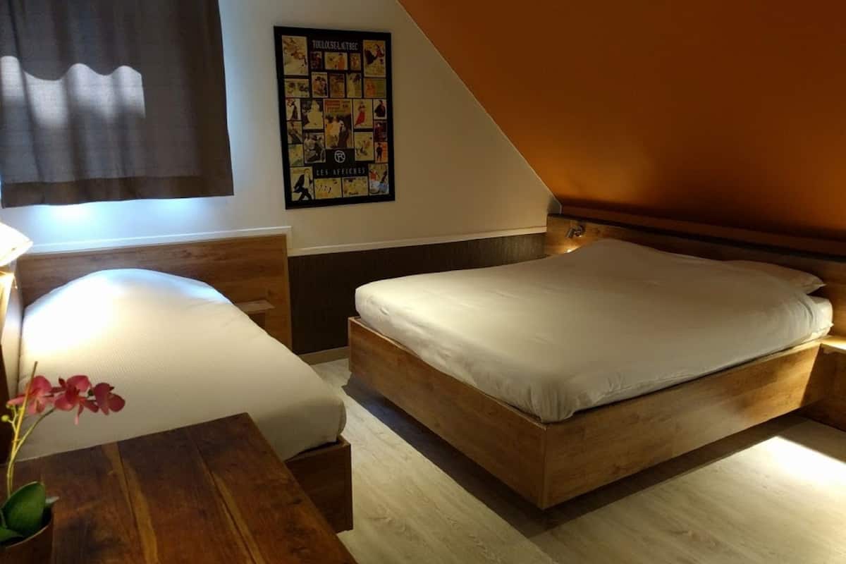 Quarto com cama de madeira, mesa de cabeceira, abajur e um cartaz na parede.