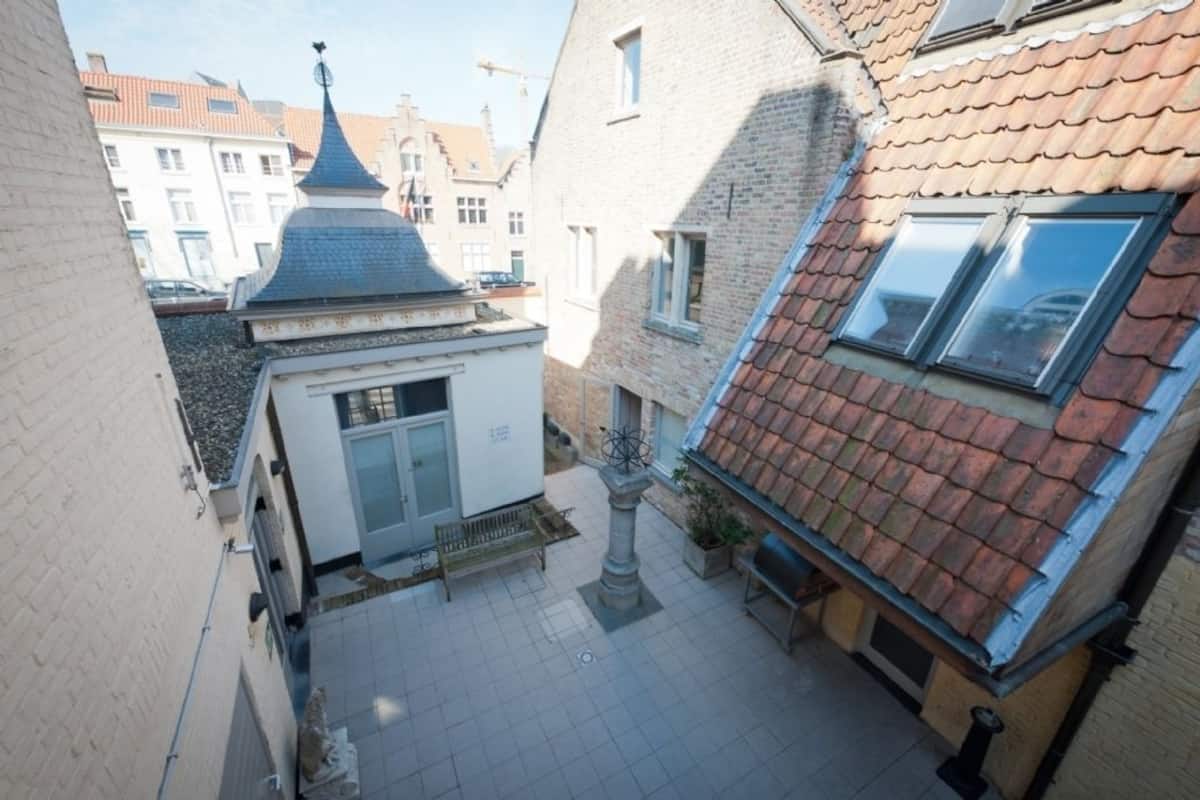 Uma passagem estreita com um pequeno edifício, teto em telhas e fachada branca.