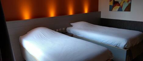 A hotel room with two single beds, a wooden headboard, and a colorful abstract painting on the wall.
