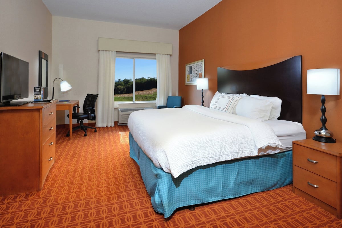A hotel room with a large bed, a desk with a computer, a chair, and a window with curtains.