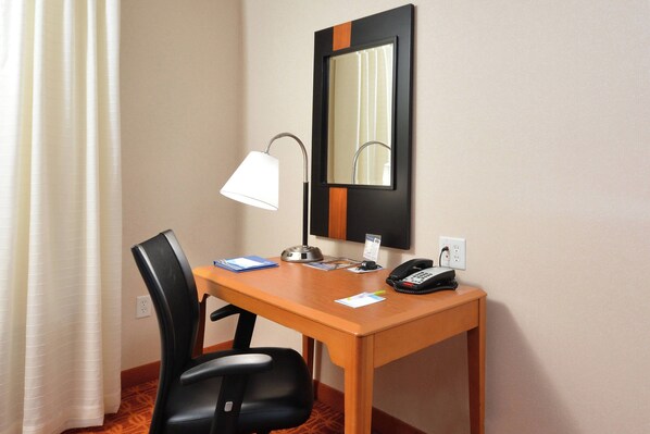 Una habitación de hotel con un escritorio de madera, una silla de oficina negra, una lámpara de escritorio, un teléfono y un espejo.