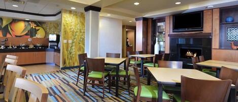 A restaurant with wooden chairs and tables, a TV mounted on the wall, and a fireplace.