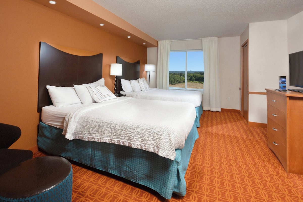 A hotel room with two beds, a TV, a desk, and a view of the outdoors.