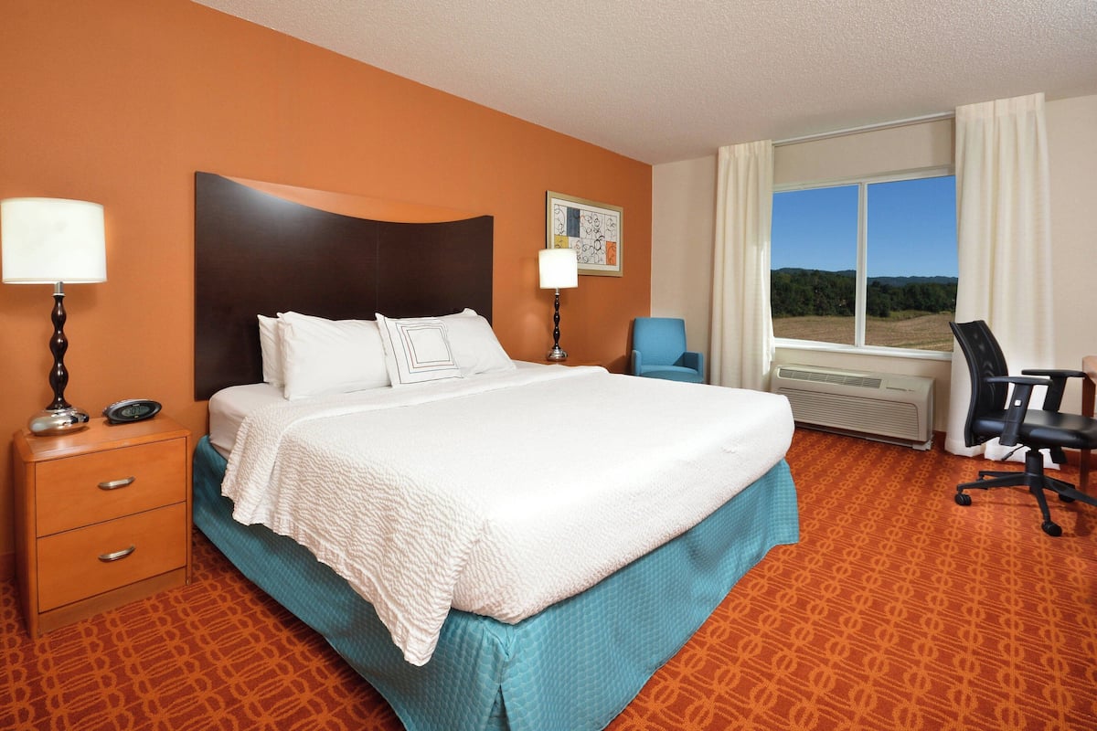 A hotel room with a large bed, two bedside tables with lamps, a desk with a chair, and a window with a view of the outdoors.