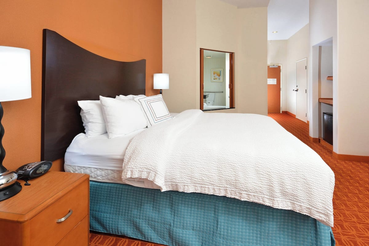 A hotel room with a large bed, a nightstand with a lamp, and a mirror on the wall.