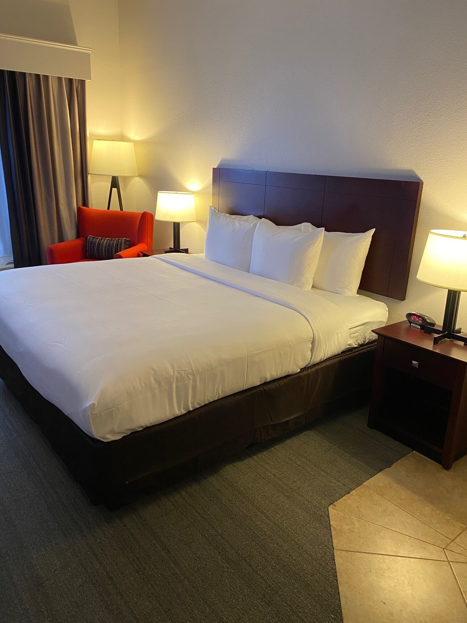 A hotel room with a large bed, two bedside tables, a red armchair, and a lamp.