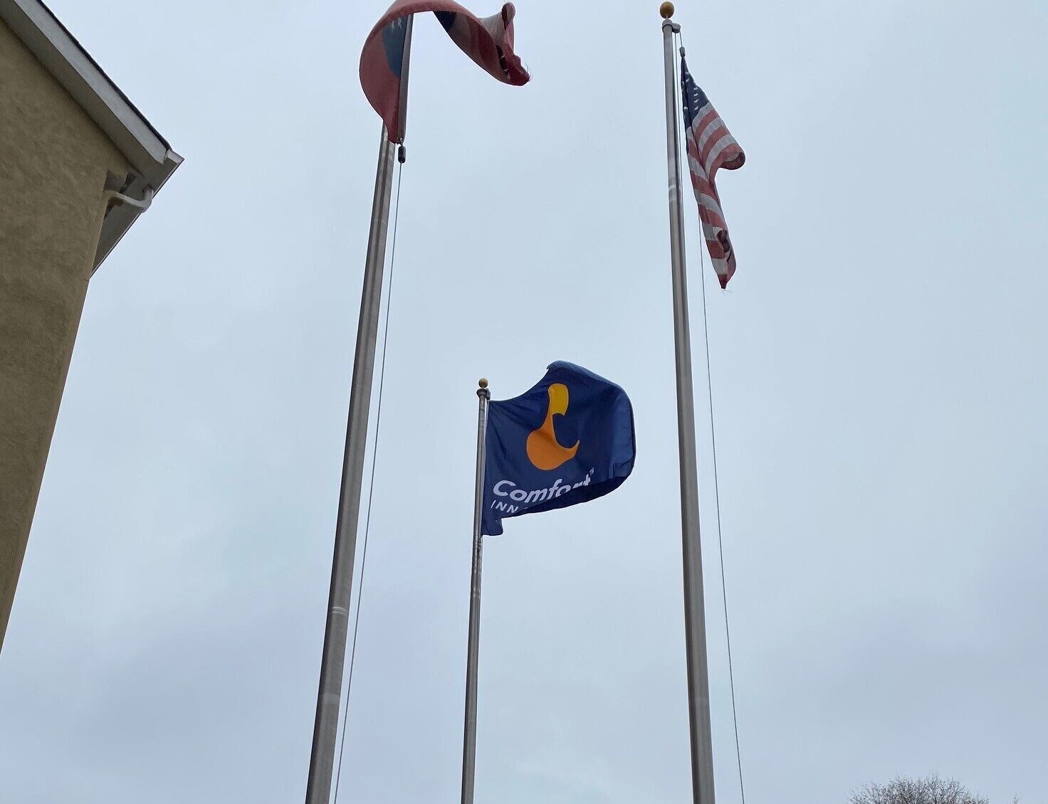 A hotel flagpole with a blue flag featuring a yellow logo, an American flag, and a red flag.