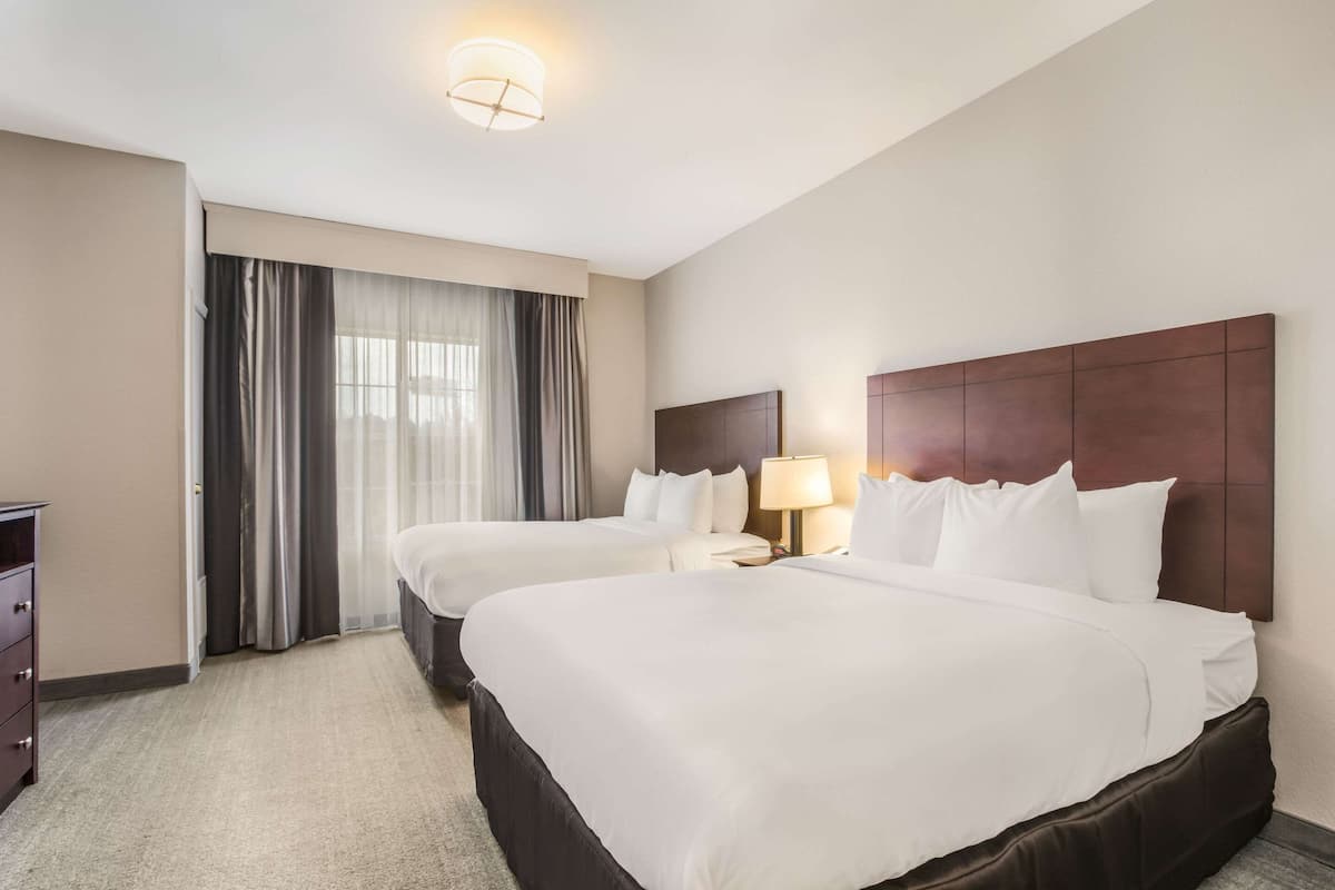 Une chambre d’hôtel avec deux lits, un bureau, une chaise, une lampe et une fenêtre avec des rideaux.