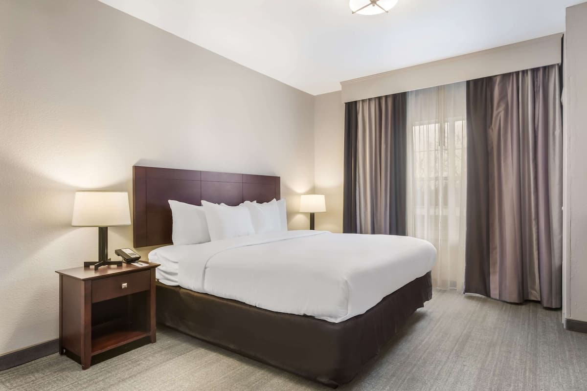 Une chambre d’hôtel avec un grand lit, deux tables de chevet avec des lampes, une tête de lit et une fenêtre avec des rideaux.