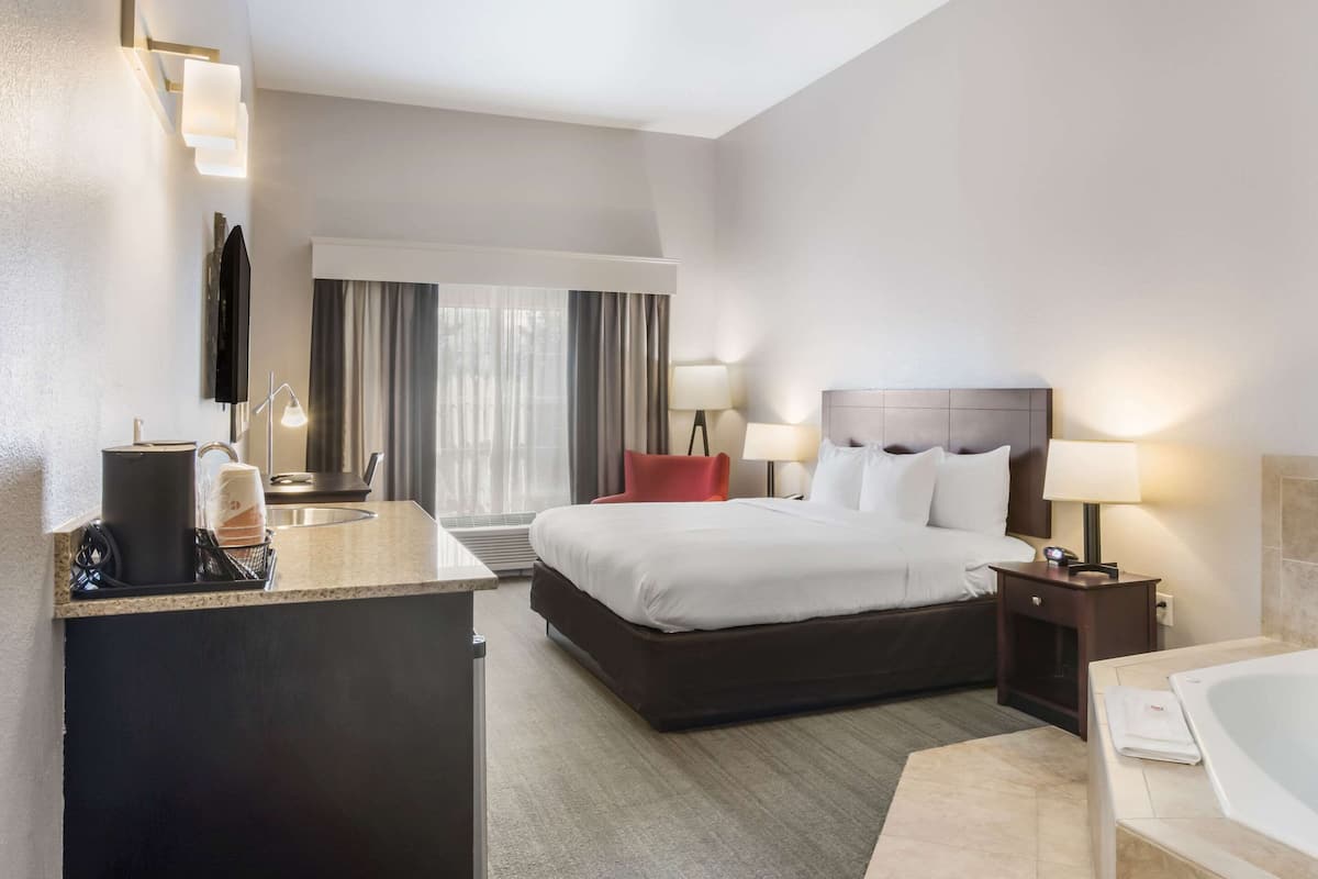 Une chambre d’hôtel comprenant un lit, des lampes de chevet, un bureau avec une machine à café, une télévision et une salle de bain avec une baignoire.