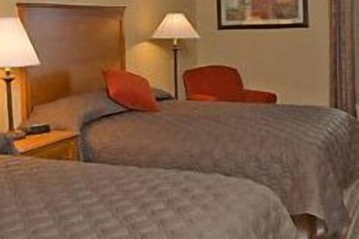 A hotel room with two beds, each with a pillow and a bedside table with a lamp.