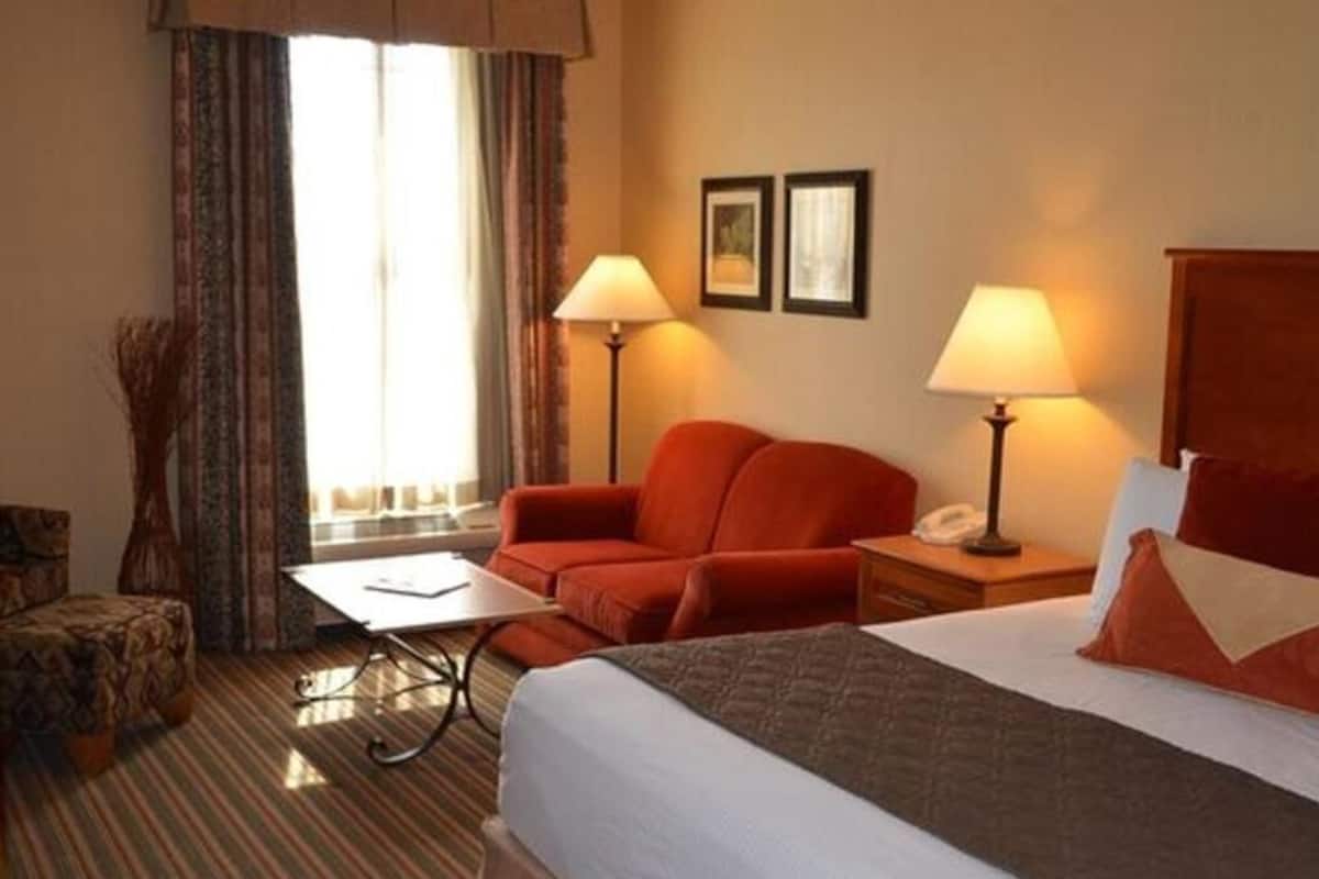 A hotel room with a bed, two bedside tables, a desk, a chair, and a window with curtains.