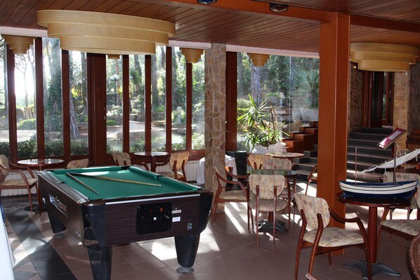 A pool table in a room with wooden pillars and chairs, a small boat, and a staircase leading to an outdoor area.