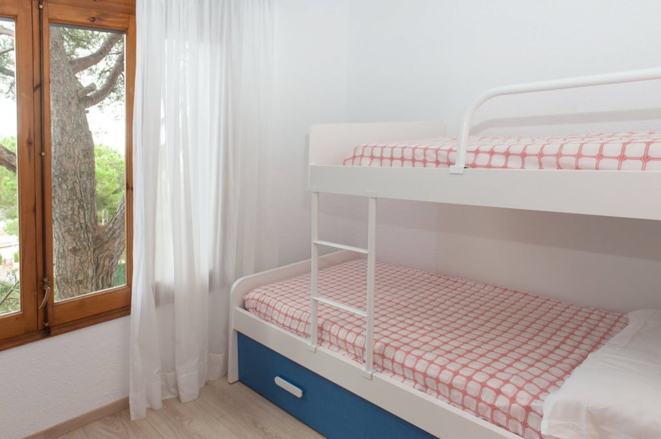 A bunk bed with a white frame and red and white checkered bedding.