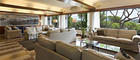 A spacious living room with multiple sofas and a large window offering a view of trees and hills.