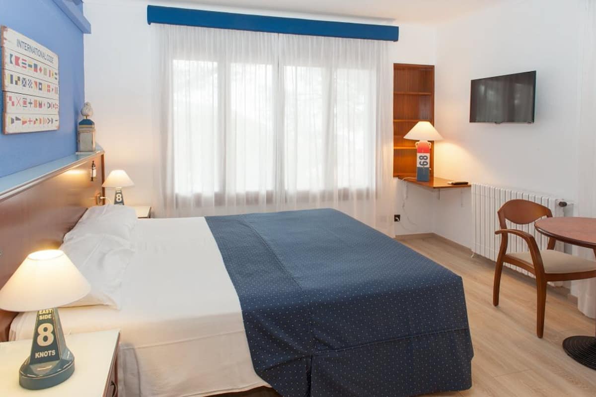Ein Hotelzimmer mit Bett, Schreibtisch, Sessel, Fernseher und einem Fenster mit Vorhängen.