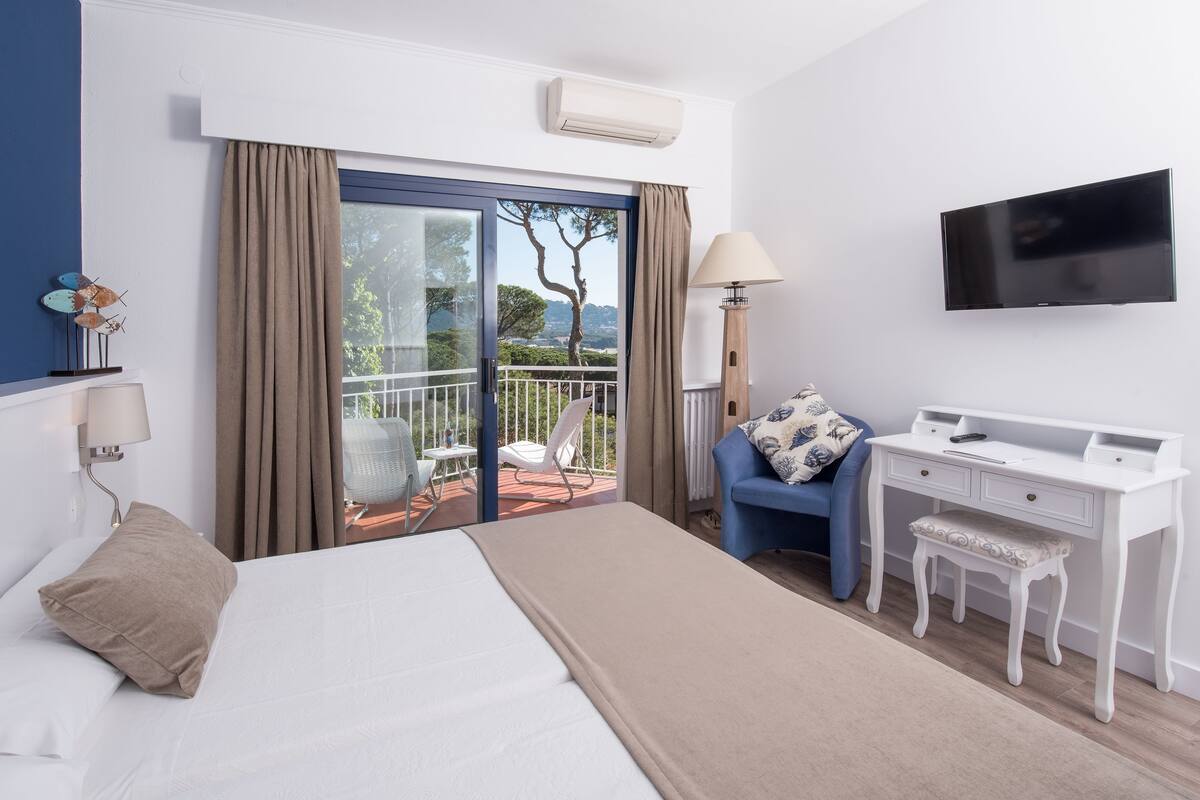 Ein Hotelzimmer mit Bett, Schreibtisch, Stuhl, Fernseher und einem Balkon mit Aussicht.