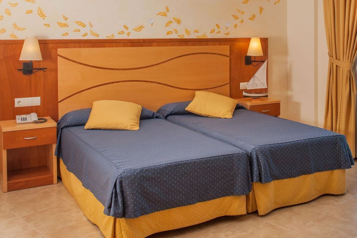 Ein Doppelbett mit Holz-Kopfschild, zwei Nachttische mit Lampen und eine Wand mit Blättermotiv.
