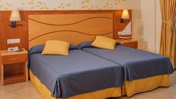 A double bed with two pillows, a wooden headboard, bedside lamps, a nightstand, and a wall with leaf decals.